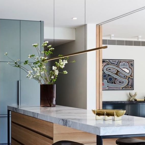Highline Linear Pendant in Patina Brass over Marble Kitchen Island with Flowers and Art